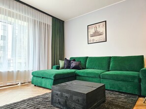 A green sofa, a dark wooden coffee table, and a window with sheer curtains.