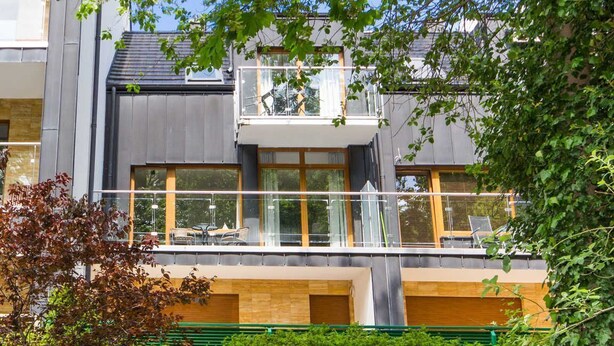 En modern byggnad i två våningar med en balkong, stora fönster och ett platt tak.