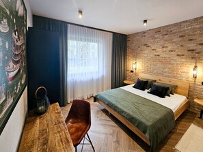 Une chambre d’hôtel moderne avec un grand lit, un bureau en bois, une chaise et un mur en briques.