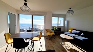 Un salon moderne avec un coin repas, de grandes fenêtres et une vue sur la mer.