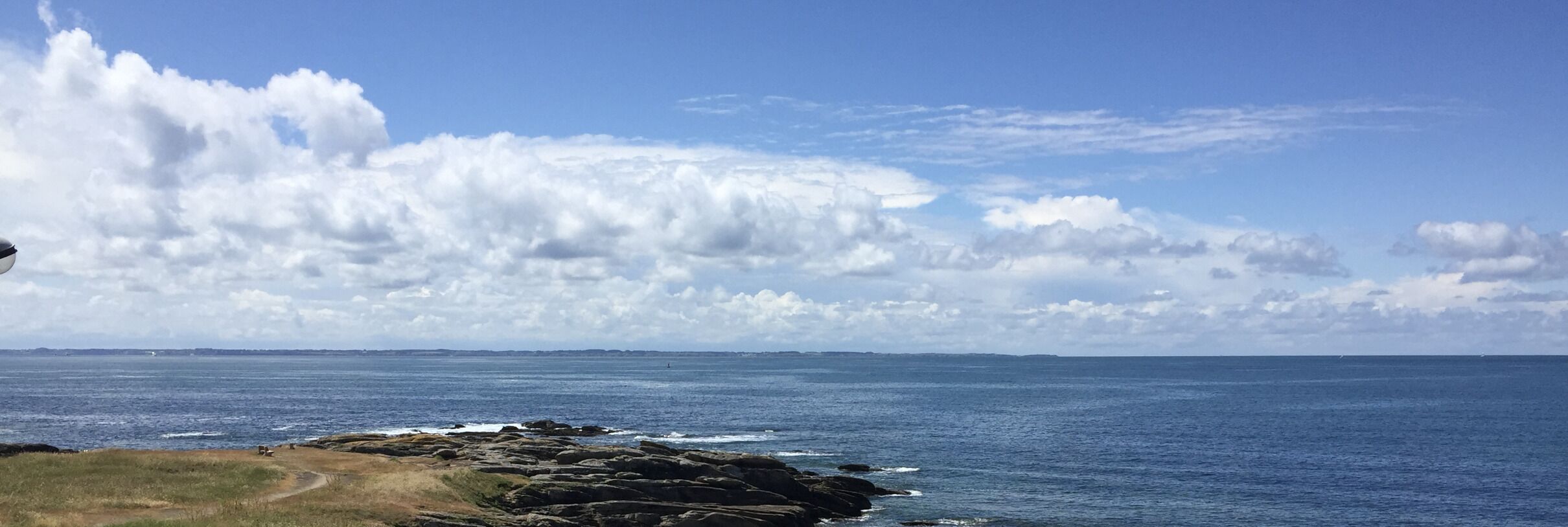 Un paisaje costero con terreno rocoso y vista al mar bajo un cielo parcialmente nublado.