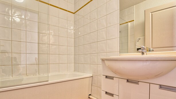 A bathroom with white tiles, a bathtub, a sink, and wooden flooring.
