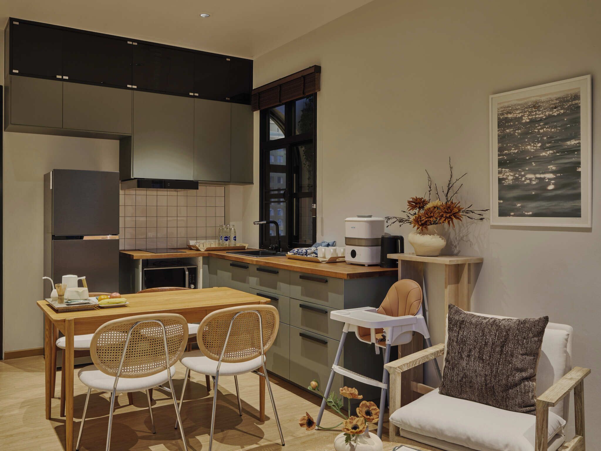 A modern kitchen with a dining area, including a wooden table, two chairs, a high chair, and a sofa.