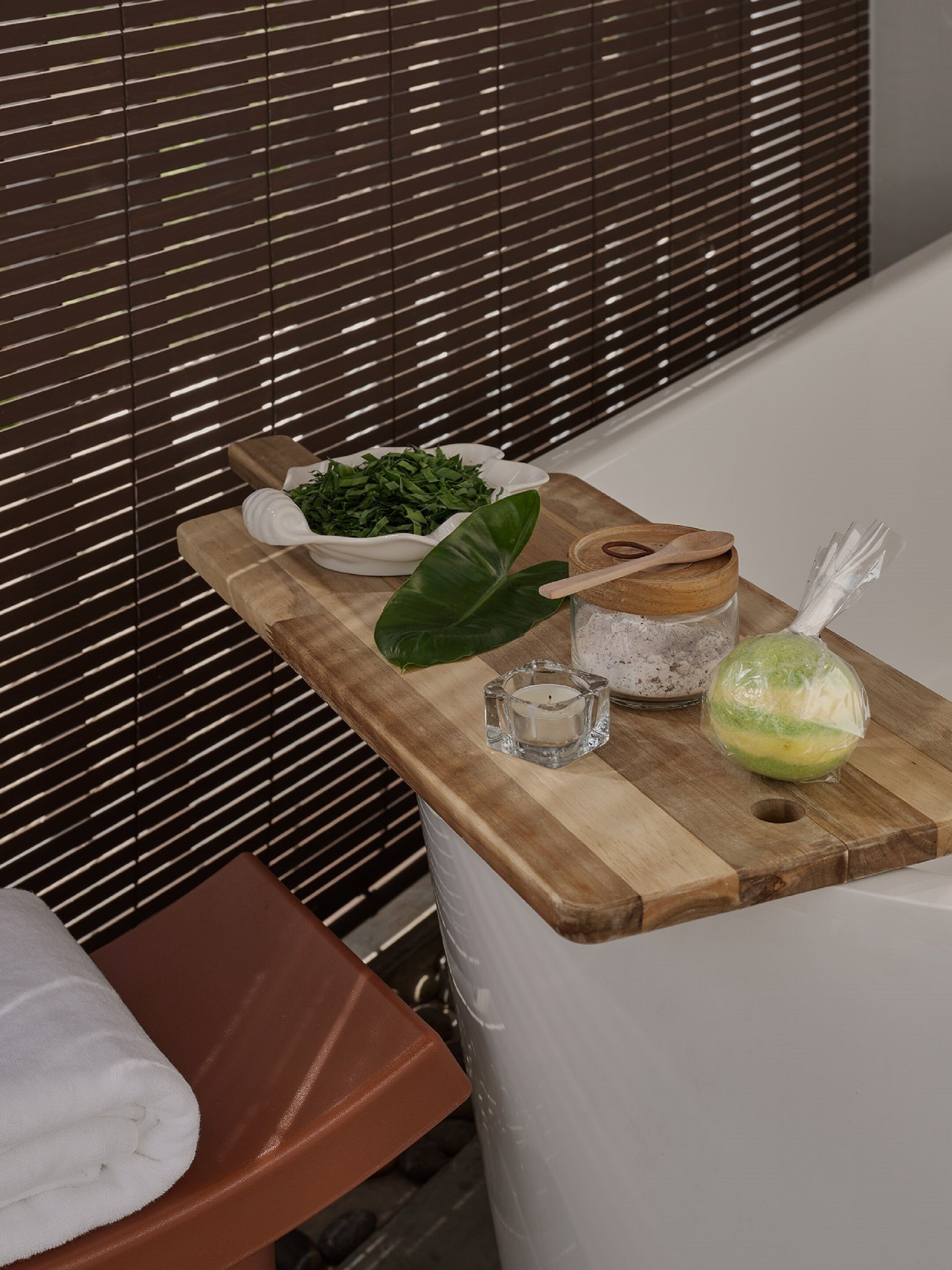 A wooden table with a bowl of greens, a candle, and a jar with a wooden lid.