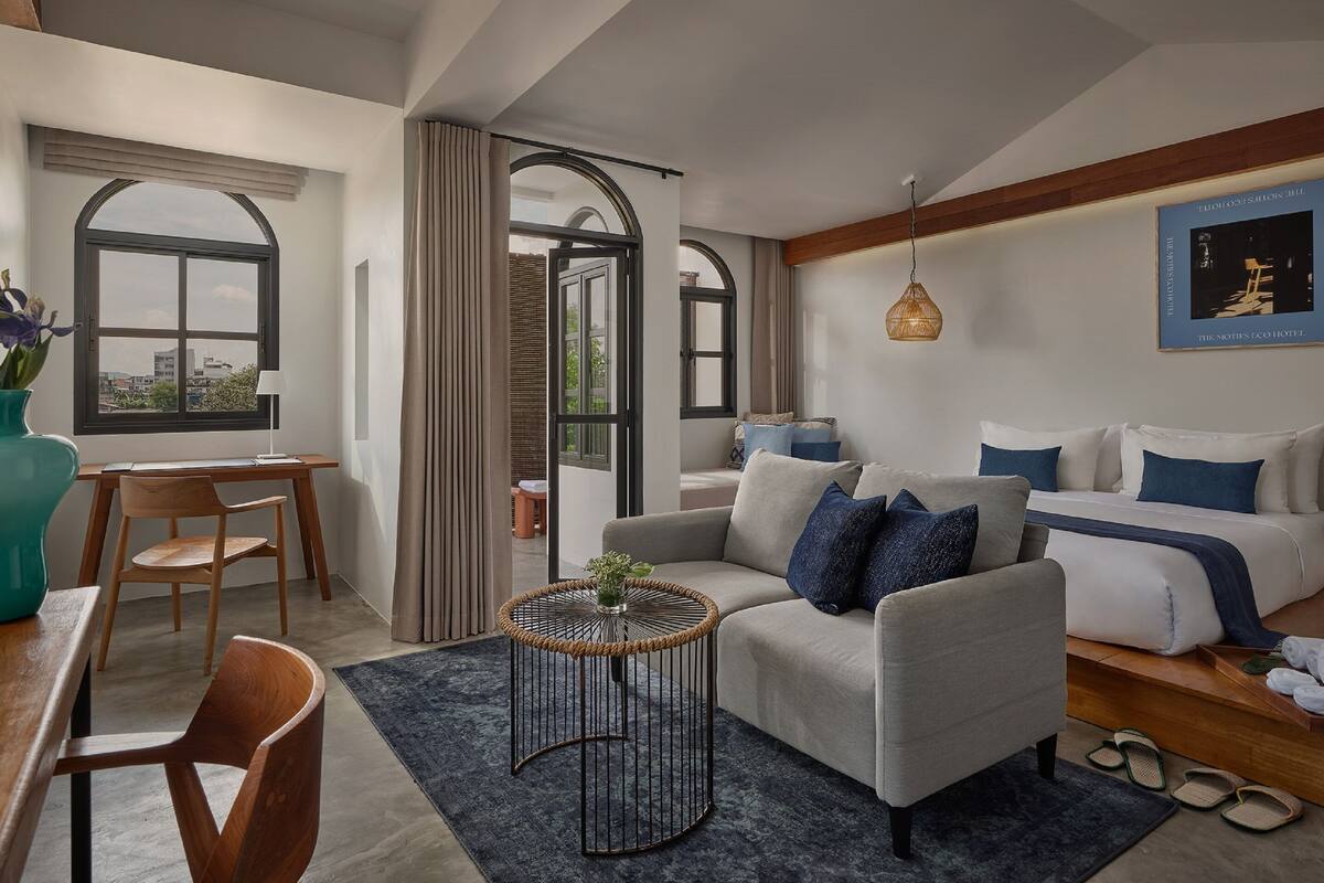 Un salon moderne avec un canapé, un coin repas comprenant une table et des chaises, et une vue sur l’extérieur grâce à de grandes fenêtres.