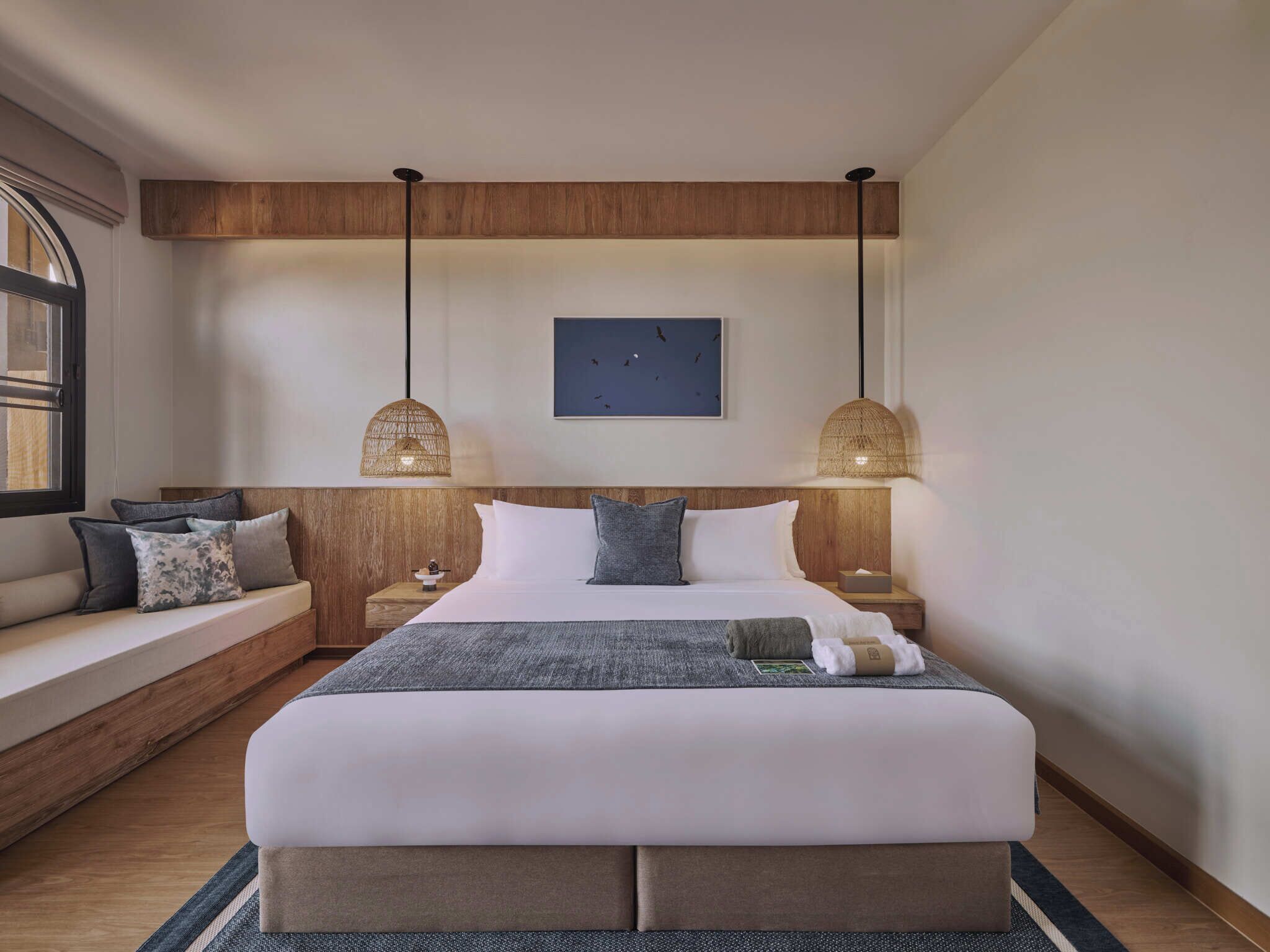 A modern bedroom with a large bed, two bedside tables, a bench, and a hanging light fixture.
