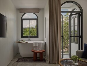 A modern bathroom with a freestanding bathtub, a window with a view of greenery, and a door leading to an outdoor area. - The Motifs Eco Hotel (Chanthaburi)