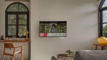 A modern hotel room with a large arched window, a desk with a vase of flowers, a comfortable sofa, and a wall-mounted TV displaying a welcome message.