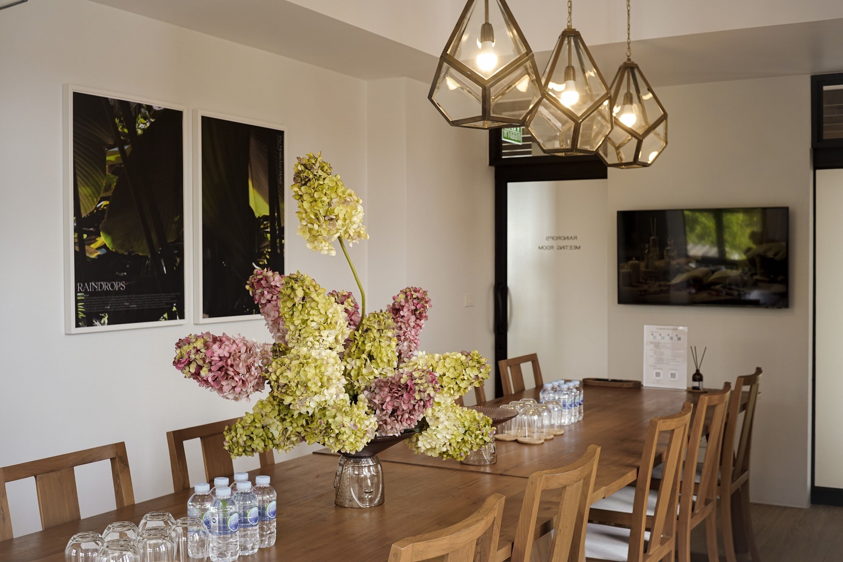 A dining area with a wooden table, chairs, a vase of flowers, and a chandelier.