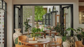 A dining area with a table set for two, surrounded by large potted plants and wooden chairs. - The Motifs Eco Hotel (Chanthaburi)