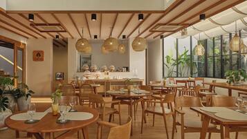 Interior moderno de restaurante com mobiliário de madeira, luminárias de vime suspensas e grandes janelas que permitem a entrada de luz natural.