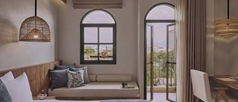 A hotel room with a bed, a seating area with a view, a desk, and a large window.
