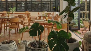 A spacious dining area with wooden tables and chairs, surrounded by large windows and indoor plants. - The Motifs Eco Hotel (Chanthaburi)
