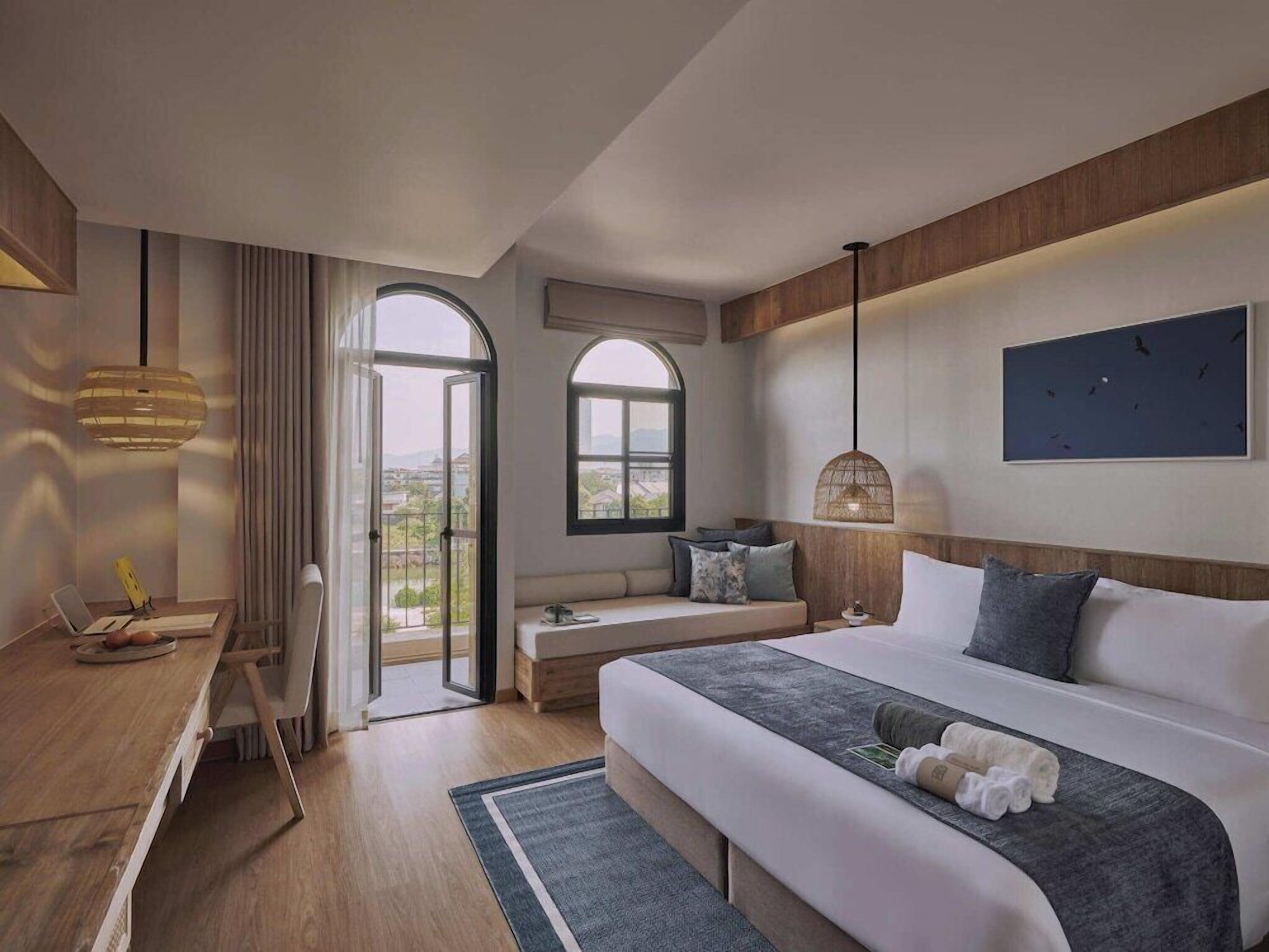 A hotel room with a bed, a desk, a chair, a window, and a view of the outside.