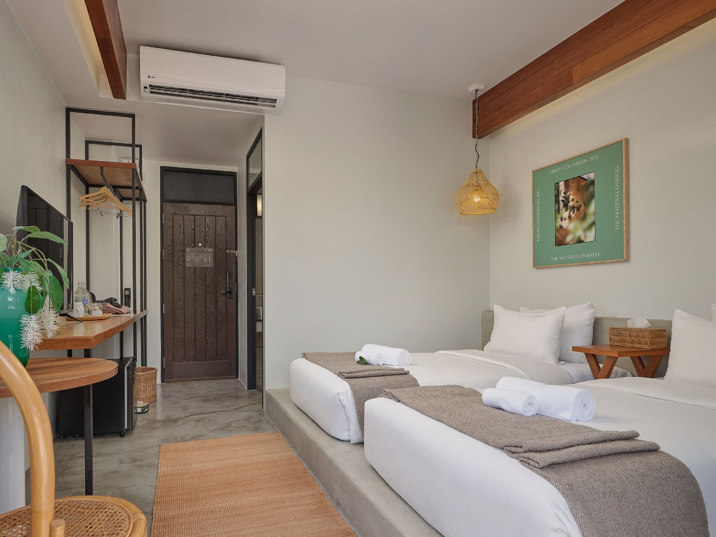 A modern hotel room with a bed, two bedside tables, a hanging light fixture, and a framed picture on the wall.