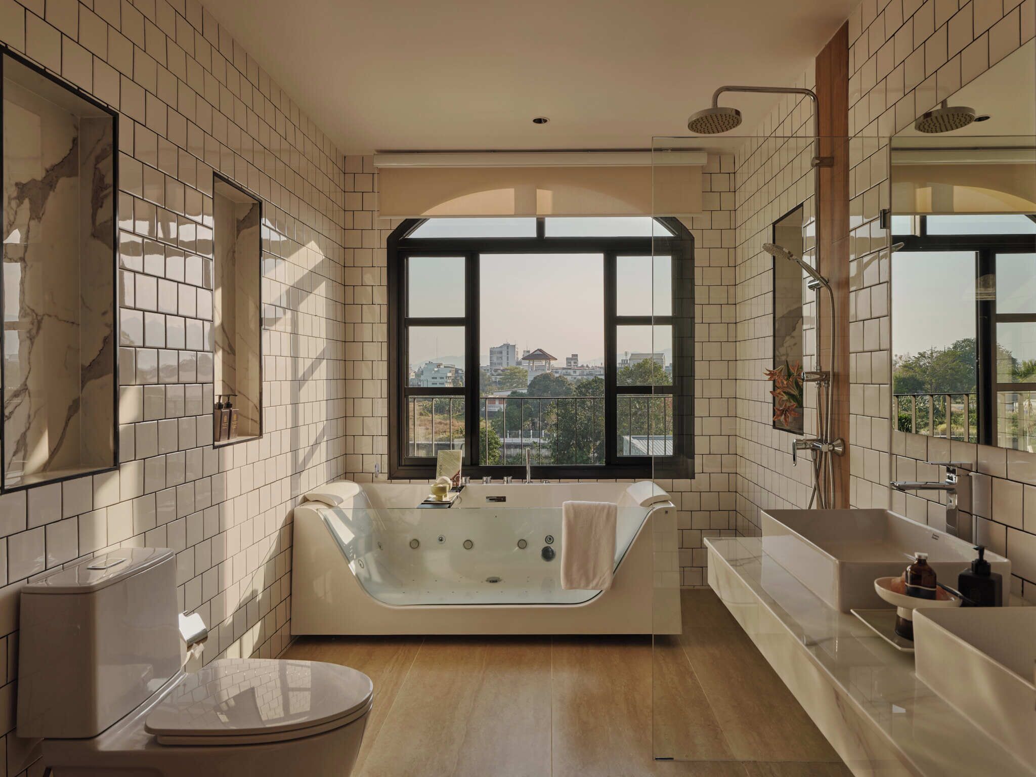 A modern bathroom with a freestanding bathtub, a large window offering a city view, and a vanity with a sink and mirror.