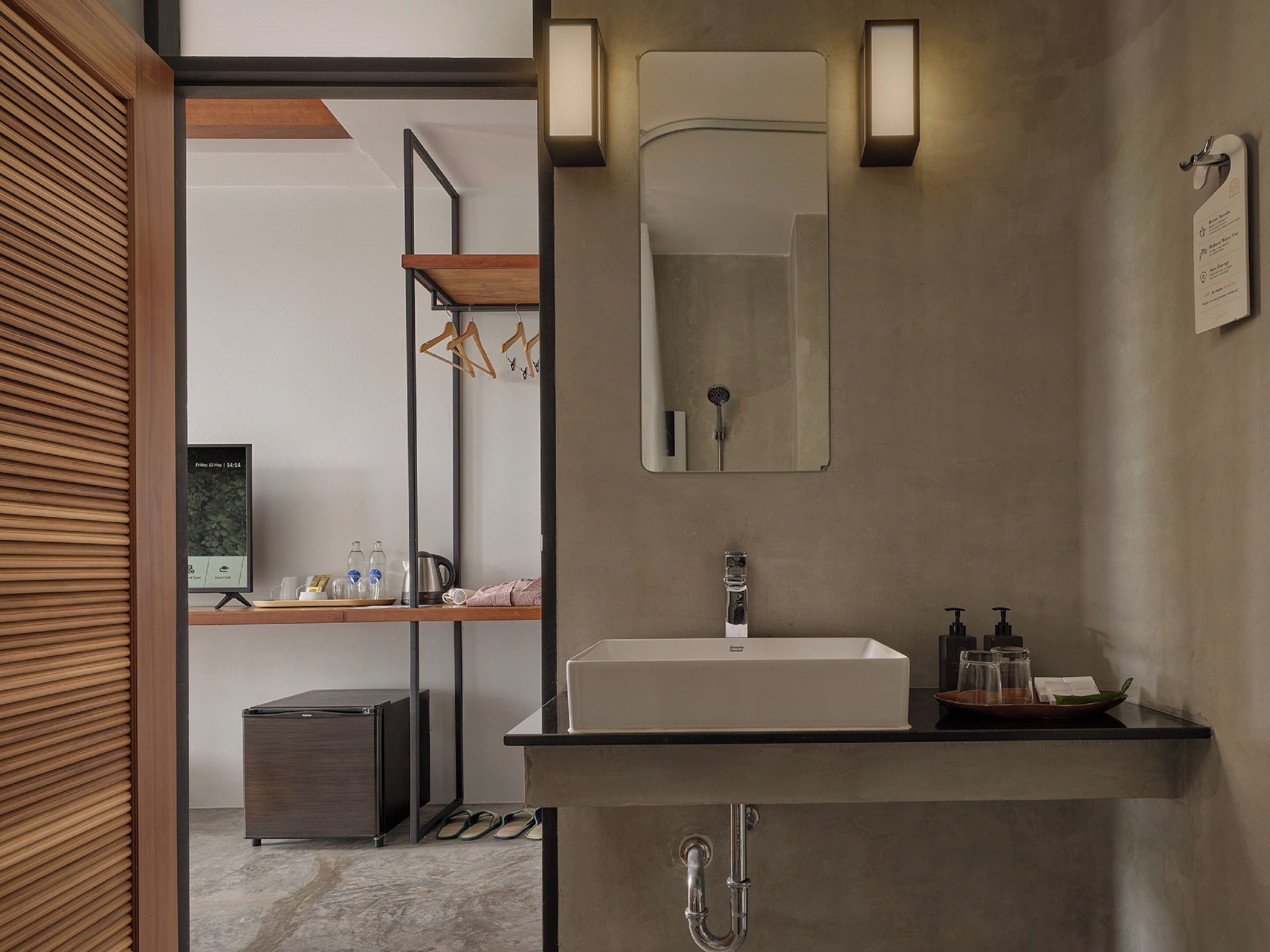 A modern bathroom with a large mirror, a sink, and a shower. There is a shelf with toiletries and a small cabinet.
