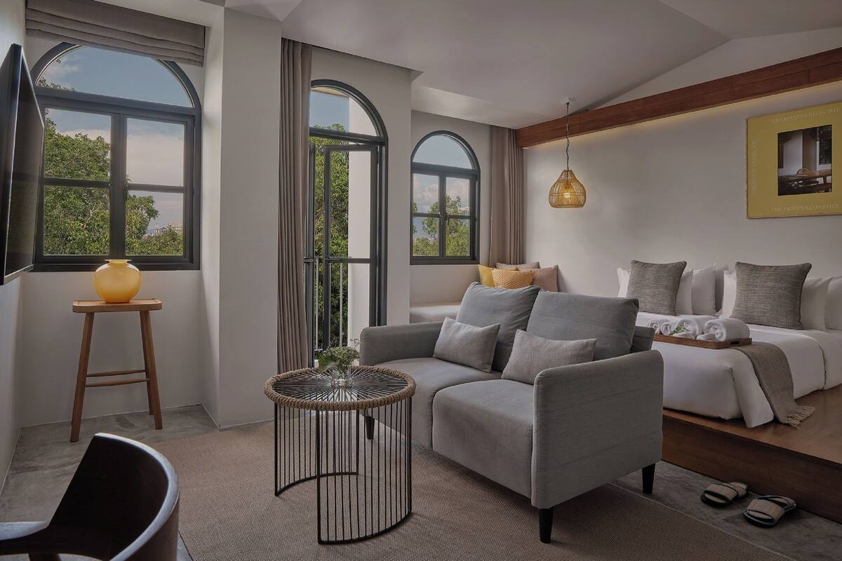 Un salon moderne avec un canapé gris, une table basse ronde et un lit recouvert de linge de lit blanc.