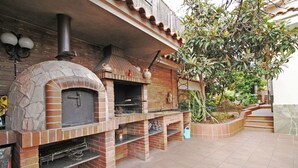 Ein outdoor-Backofen mit Steinverkleidung und Schornstein, umgeben von einer gefliesten Terrasse und einem kleinen Garten.
