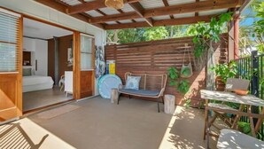 A covered patio area with a wooden bench, a table, and a bed visible through an open door. - Boudoir on Bryce St - (Pet Friendly to ONE, SMALL non hair shedding dog 4.5kg) (Moffat Beach)