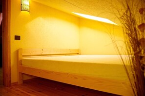A single wooden bed in a room with yellow walls and a ceiling light. - Villa With Sauna and hot tub on the Lakeshore (Kuliai)