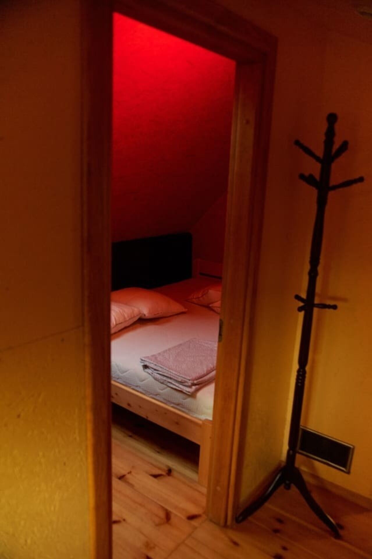 A narrow doorway leading to a bedroom with a bed, a coat rack, and a red light.