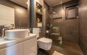 Une salle de bain moderne avec un grand lavabo blanc, des toilettes et une douche séparée par une paroi de verre.
