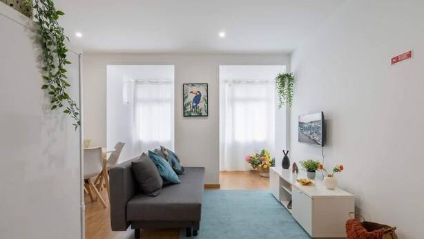 Ein modernes Wohnzimmer mit einem grauen Sofa, einem kleinen Teppich, einem weißen Schrank und einem Fernseher an der Wand.