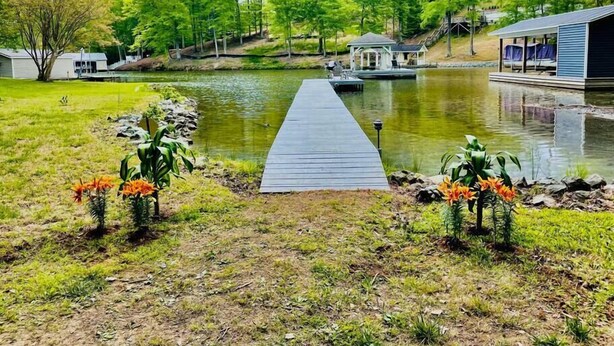 Um píer de madeira se estende sobre um lago tranquilo, cercado por vegetação exuberante e um gazebo.