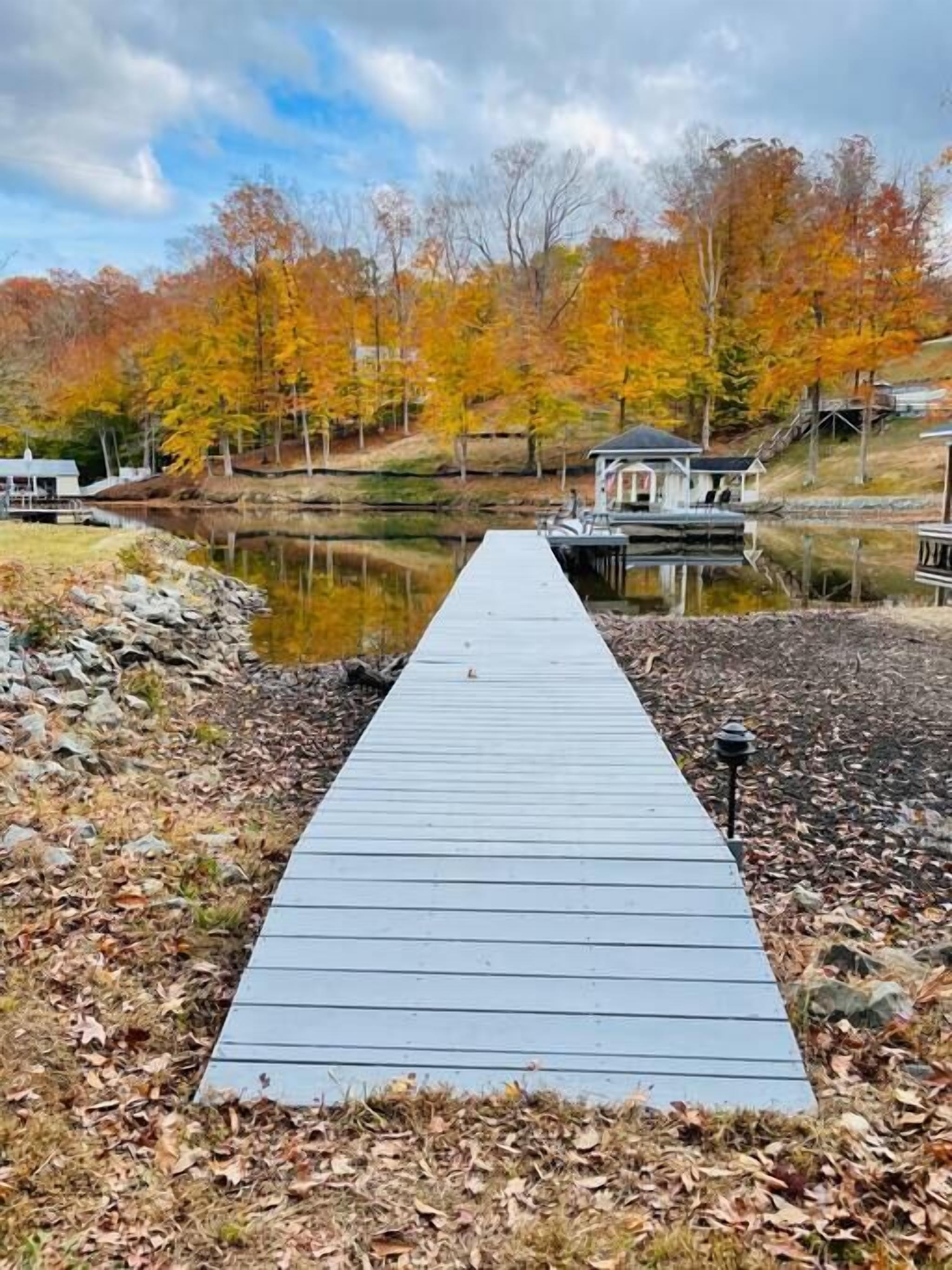 Eine Holzsteg, der zu einem kleinen Haus am See mit Herbstlaub führt.