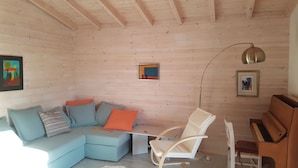 Een gezellige woonkamer met een lichtblauwe modulaire bank, een witte schommelstoel, een houten piano en een vloerlamp.