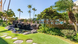 A landscaped garden with a rock formation, palm trees, and a pool area. - Sugar Beach PH21 - Direct Oceanfront 1 bedroom (Kihei)