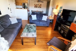 Una sala de estar con sofá, mesa de centro, televisor y una cocina al fondo.