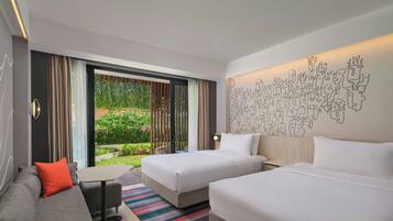A hotel room with two beds, a sofa, a small table, and a view of a garden through large windows.