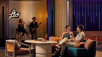 Une scène avec un groupe de musique, un panneau lumineux au néon et un espace réservé aux spectateurs, avec une table et des chaises.
