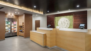 Un espace d’accueil comprenant un comptoir de réception en bois, un réfrigérateur rempli de boissons et un élément décoratif mural.