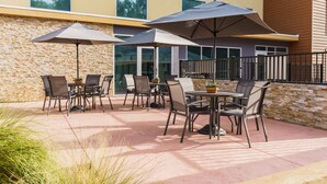 Une terrasse extérieure avec des tables et des chaises, de grands parasols et un mur en pierre.