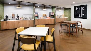 Uma sala de jantar moderna com uma mesa branca e cadeiras amarelas, uma cozinha com armários de madeira, e um letreiro na parede com a inscrição 'Hello Fall'.