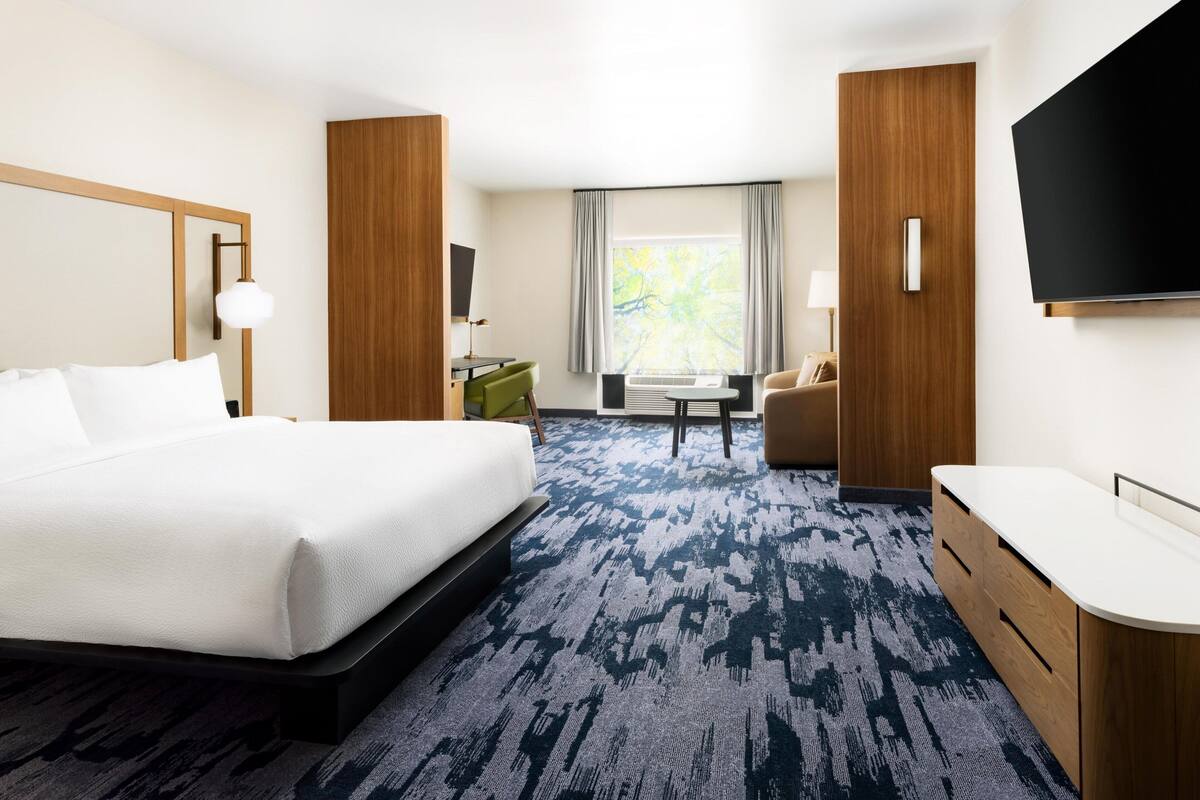 Ein Hotelzimmer mit einem großen Bett, einem Schreibtisch, einem Stuhl, einem Fernseher und einem Fenster mit Vorhängen.