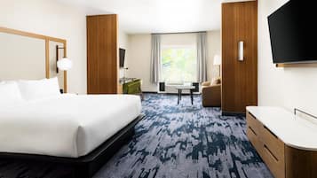 Quarto de hotel com uma cama grande, uma escrivaninha, uma cadeira, uma televisão e uma janela com cortinas.
