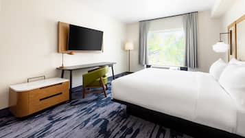 Quarto de hotel com uma cama grande, uma escrivaninha, uma cadeira, uma televisão e uma janela com cortinas.