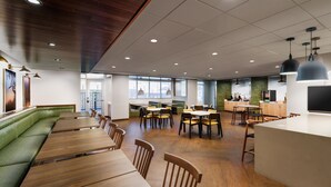 Un espace de restauration moderne avec des tables en bois, des sièges rembourrés de couleur verte et des luminaires suspendus.