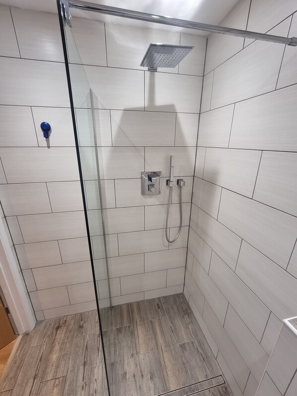 A glass-enclosed shower with a handheld showerhead and a wall-mounted faucet.