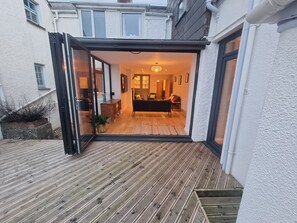 An open sliding glass door leading to a living room with a sofa, a coffee table, and a chandelier.