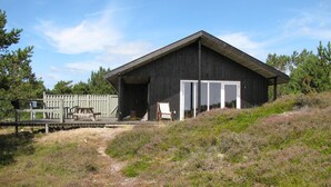 Una cabaña rústica con una puerta grande abierta, una mesa de picnic y una silla afuera.