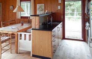 A wooden interior with a kitchen area, a dining table, and a window.