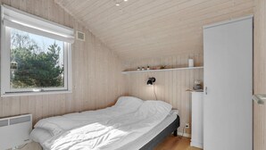 Een slaapkamer met een bed, een witte garderobe, een plank met planten, een raam en een wandlamp.