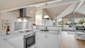 A modern kitchen with white cabinetry, stainless steel appliances, and a large window overlooking a garden.