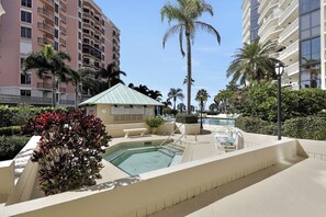 A pool area with a small gazebo, surrounded by palm trees and a building with balconies.