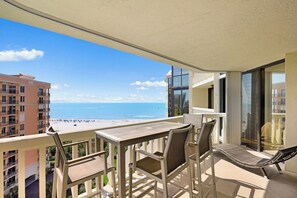A balcony with a table and chairs overlooking a beach.